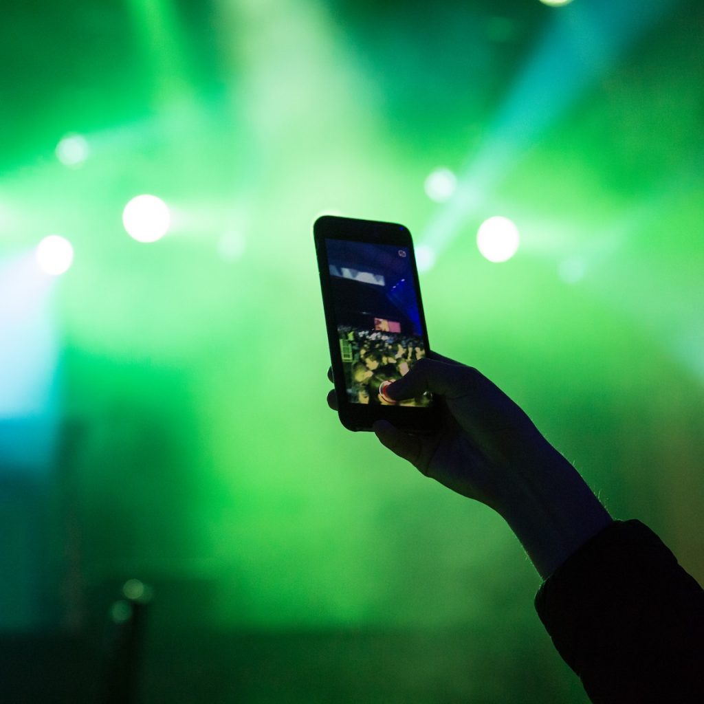 A silhouette of a hand filming a concert using an iPhone