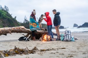 3 people and a god on the beach with a campfire