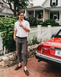 Man posed besides antique red car in front of a house.