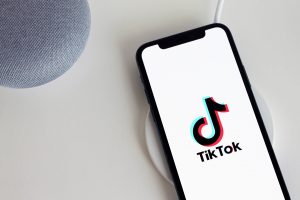 An image of a smart phone and a speaker on a table with TikTok's logo displayed on the smart phone's screen.