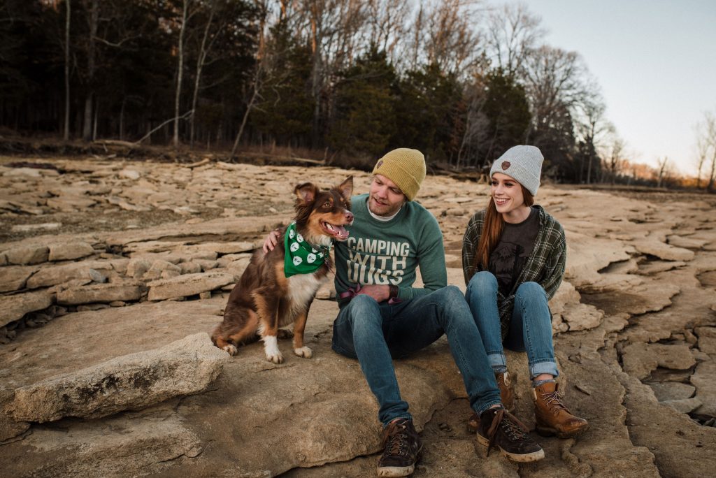A man and woman hanging out with a happy australian shepherd in nature.