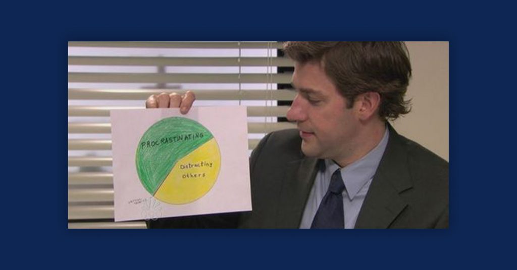 A still image of The Office television show. Jim Halpert holds a chart. This image is on a navy background.